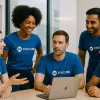 a group of people looking at a computer wearing blue custom DTF printed t-shirts with the same logo in white
